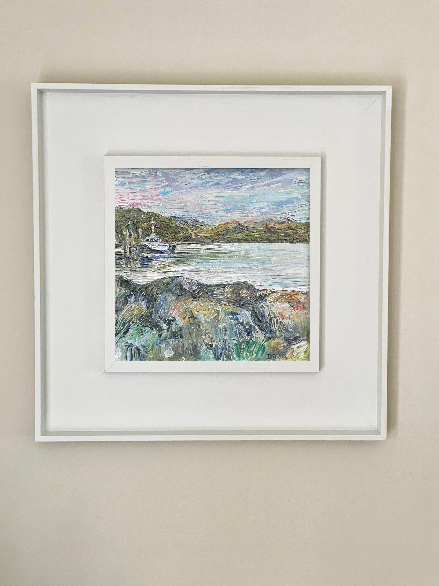 Framed painting of a coastal scene with a boat on a beige wall