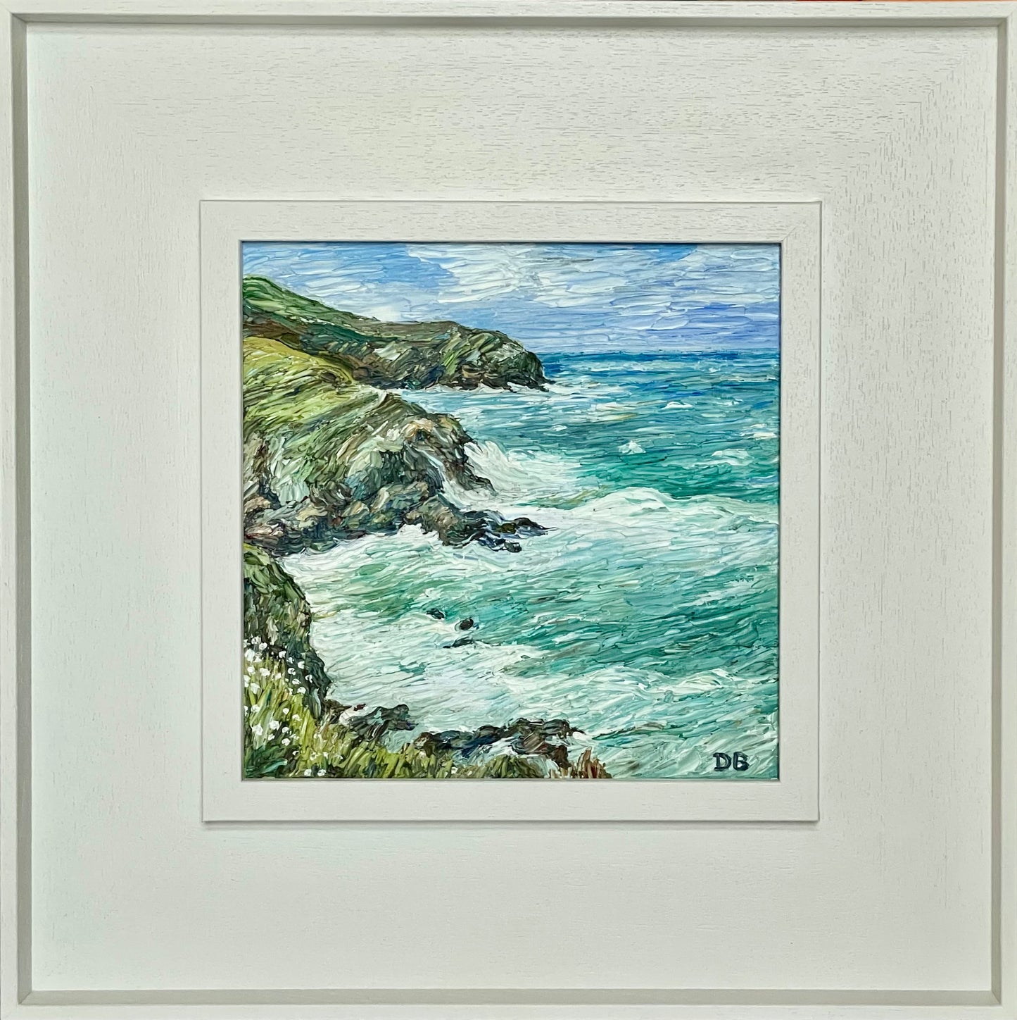 Framed artwork of a coastal scene with cliffs and ocean.