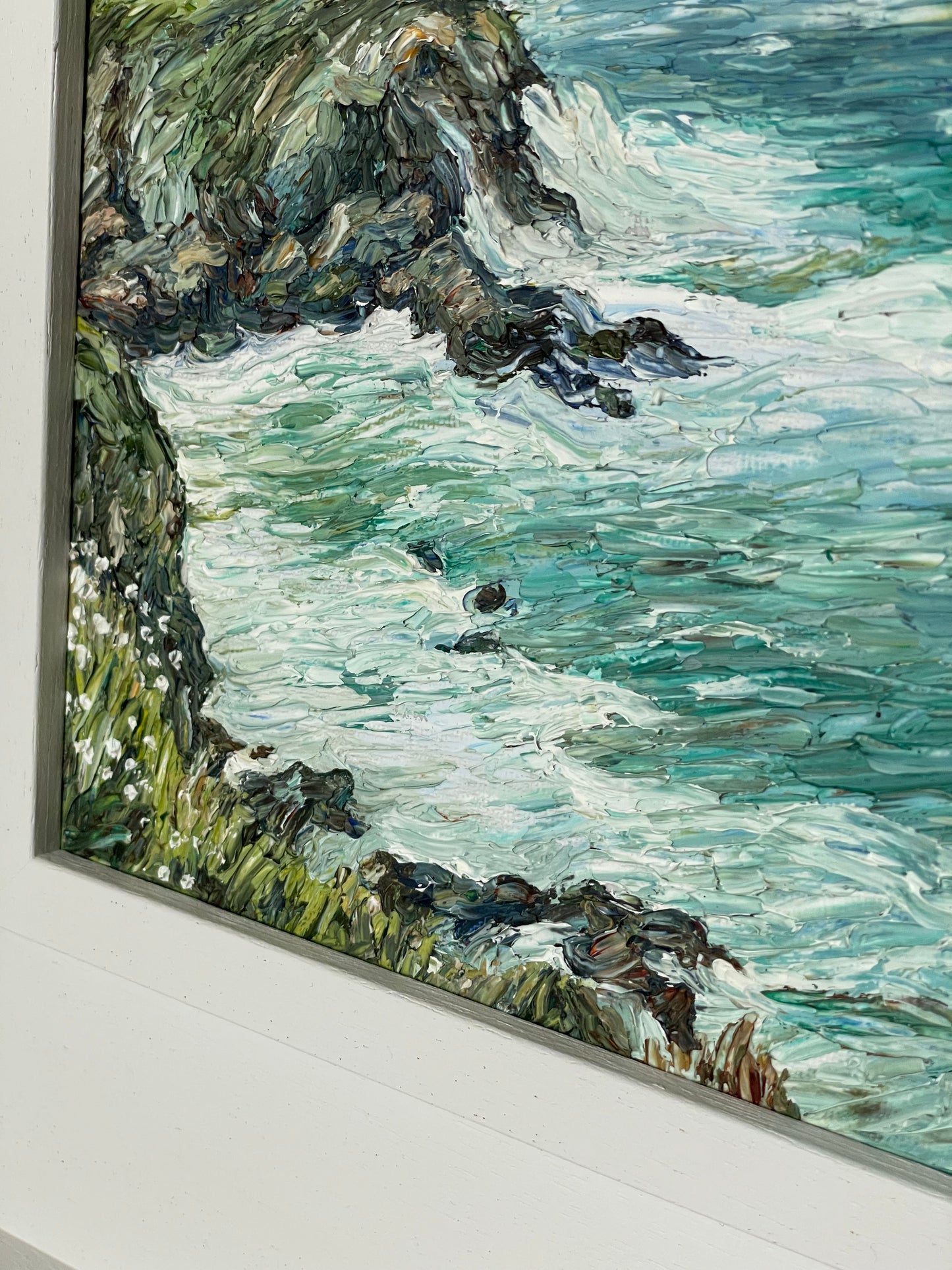 Framed painting of a coastal scene with waves crashing against rocks.