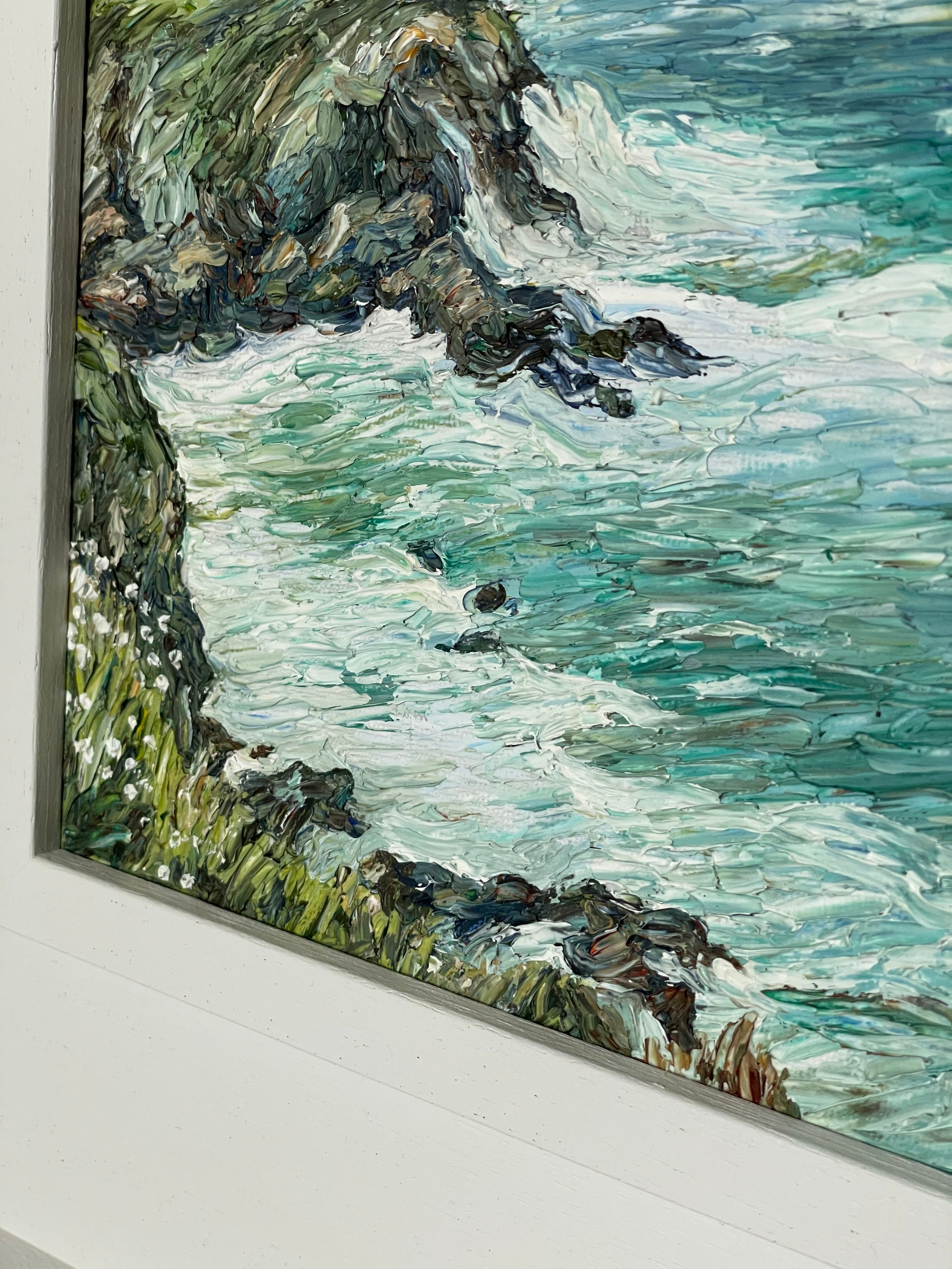 Framed painting of a coastal scene with waves crashing against rocks.