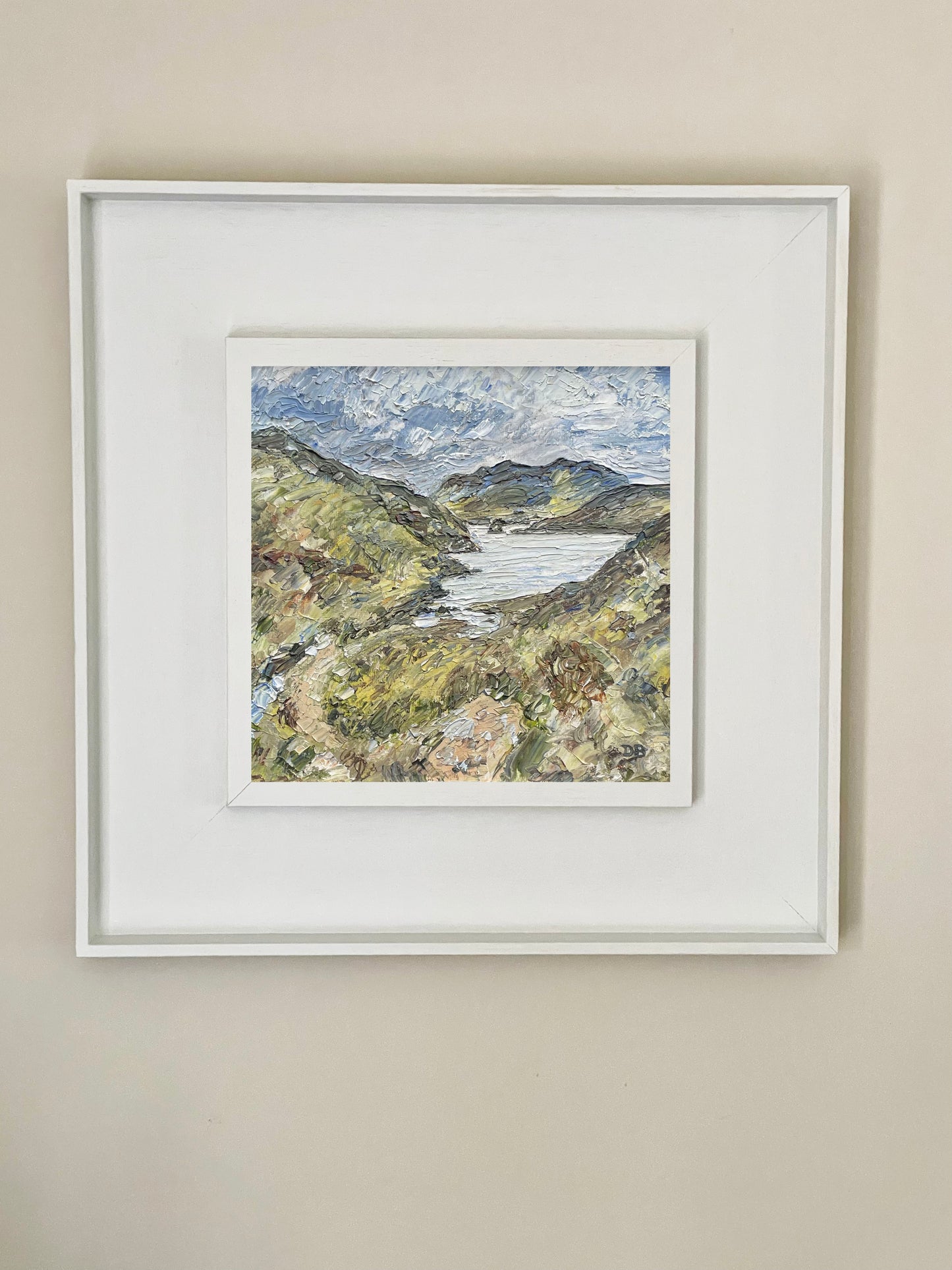 Framed artwork of a landscape with mountains and water on a beige wall.